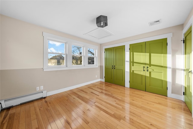 unfurnished bedroom featuring baseboard heating, light wood-type flooring, and multiple closets