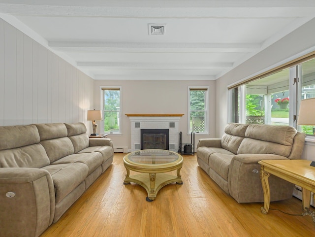 living room featuring a healthy amount of sunlight, light wood-type flooring, a brick fireplace, and beamed ceiling