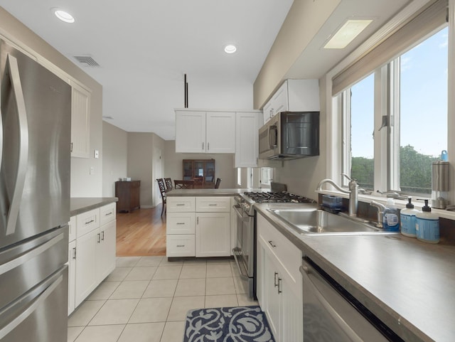 kitchen with stainless steel appliances, light tile patterned floors, white cabinets, and sink