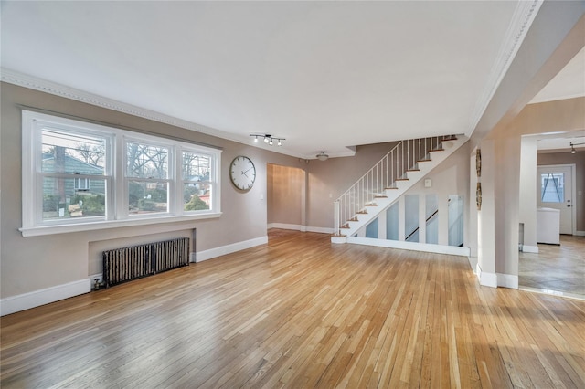 unfurnished living room with ornamental molding, rail lighting, radiator, and light wood-type flooring