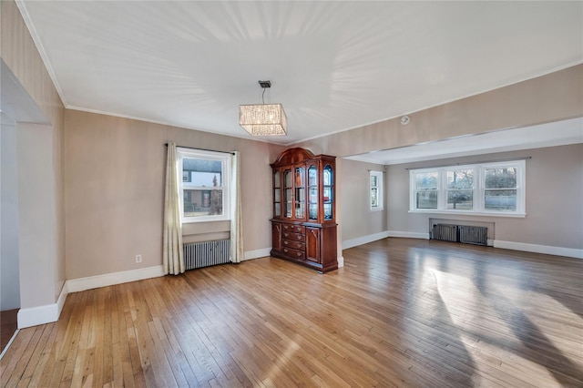 unfurnished living room featuring light hardwood / wood-style flooring, a notable chandelier, radiator heating unit, and ornamental molding