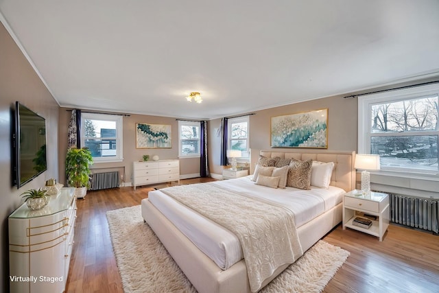 bedroom featuring ornamental molding, radiator, hardwood / wood-style floors, and multiple windows