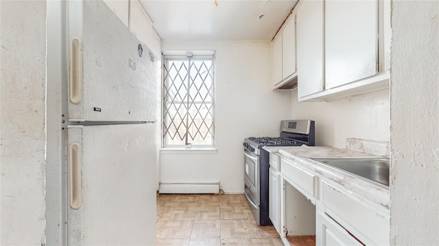 kitchen with white refrigerator, white cabinets, light parquet flooring, gas range, and baseboard heating