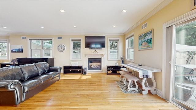 living room with recessed lighting, visible vents, light wood finished floors, a glass covered fireplace, and crown molding