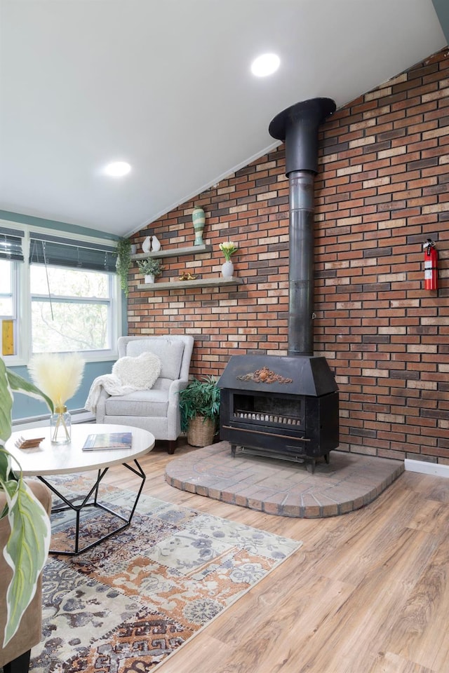 living room with brick wall, vaulted ceiling, hardwood / wood-style flooring, and a wood stove