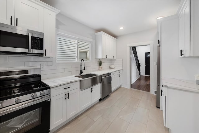 kitchen featuring light stone counters, stainless steel appliances, white cabinets, and sink