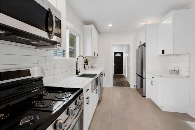 kitchen featuring sink, white cabinetry, light stone counters, tasteful backsplash, and appliances with stainless steel finishes