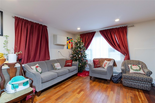 living room with baseboard heating, a wall unit AC, and wood-type flooring