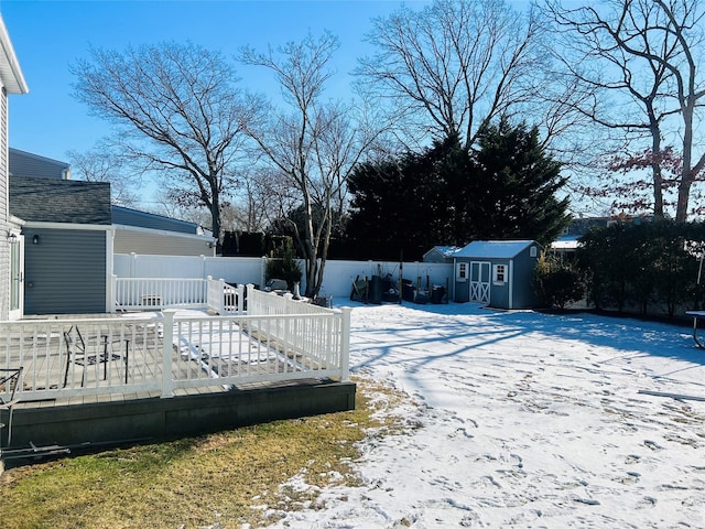 yard layered in snow featuring a wooden deck and a storage unit