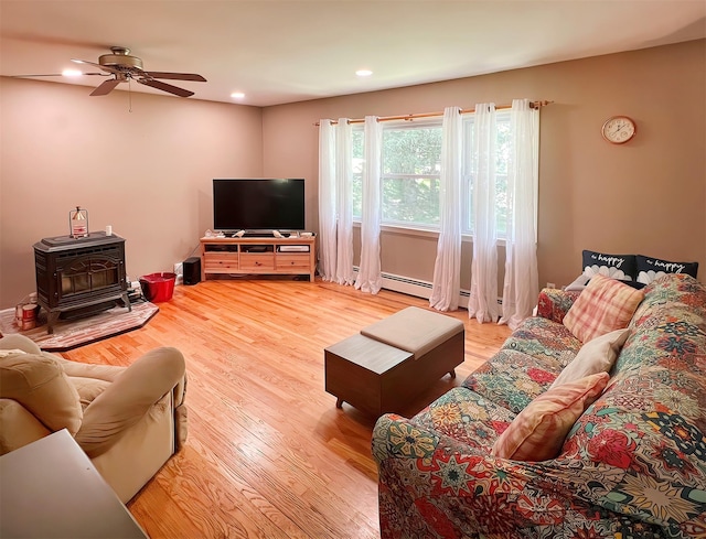 living room featuring a baseboard heating unit, ceiling fan, a wood stove, and hardwood / wood-style flooring