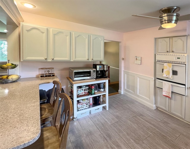 kitchen with white oven, ceiling fan, and light stone counters