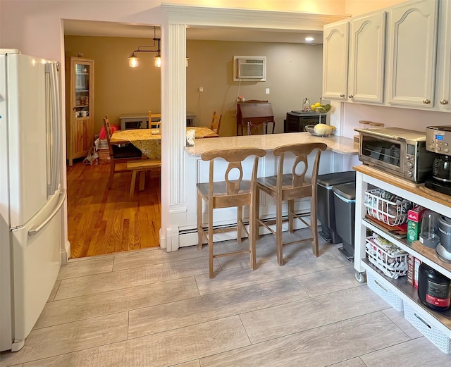 kitchen with a wall unit AC, white refrigerator, a kitchen bar, and white cabinetry