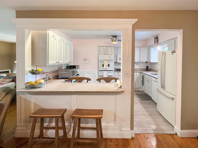 kitchen featuring a breakfast bar, white appliances, and white cabinetry