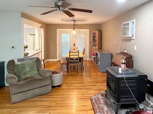 living room featuring ceiling fan, a wall mounted AC, a wood stove, and light hardwood / wood-style floors