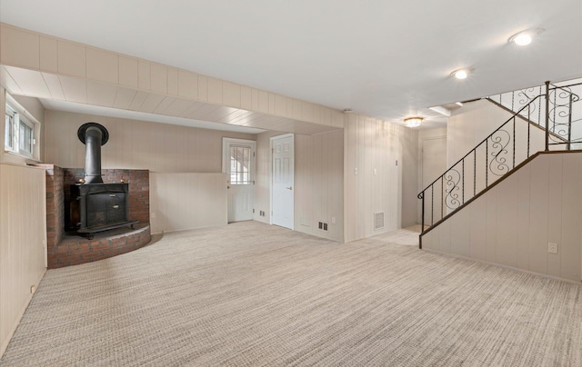 unfurnished living room with wood walls, light carpet, and a wood stove