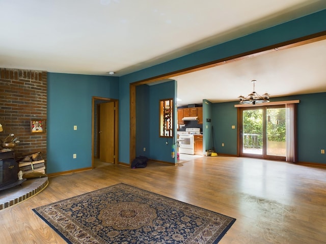 living room with light hardwood / wood-style floors, a notable chandelier, lofted ceiling, and a wood stove