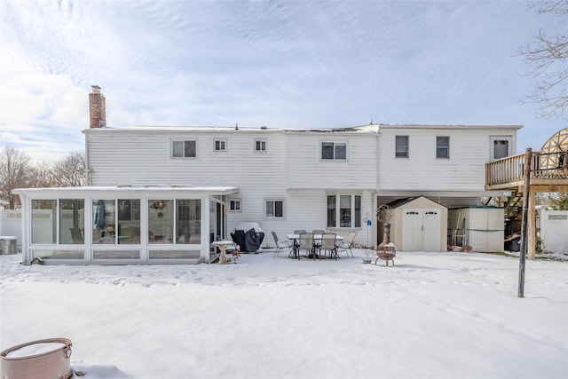 snow covered rear of property featuring a sunroom, central air condition unit, and a storage unit