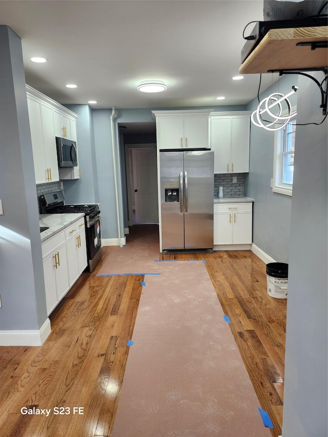 kitchen with stainless steel appliances, white cabinets, light hardwood / wood-style floors, decorative backsplash, and pendant lighting