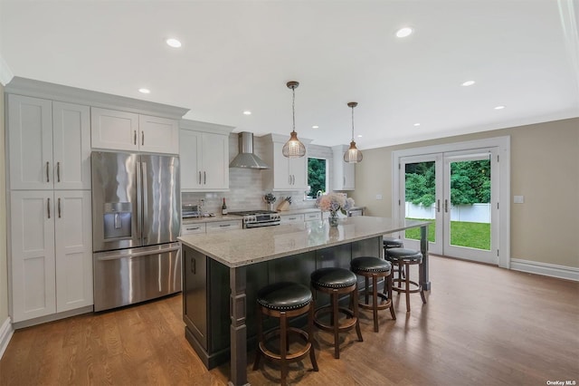 kitchen with a kitchen island, light stone countertops, appliances with stainless steel finishes, and wall chimney range hood