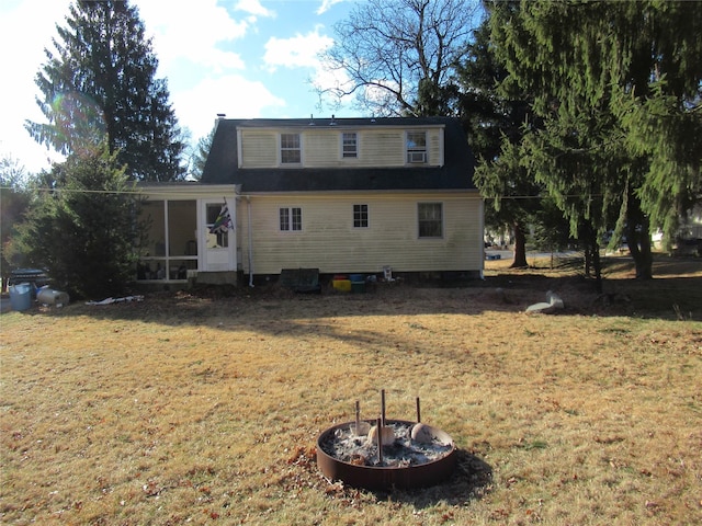 back of property featuring a fire pit, a sunroom, and a lawn