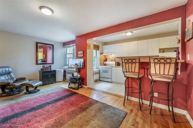 kitchen with white cabinets, light hardwood / wood-style floors, a kitchen bar, and white gas stove