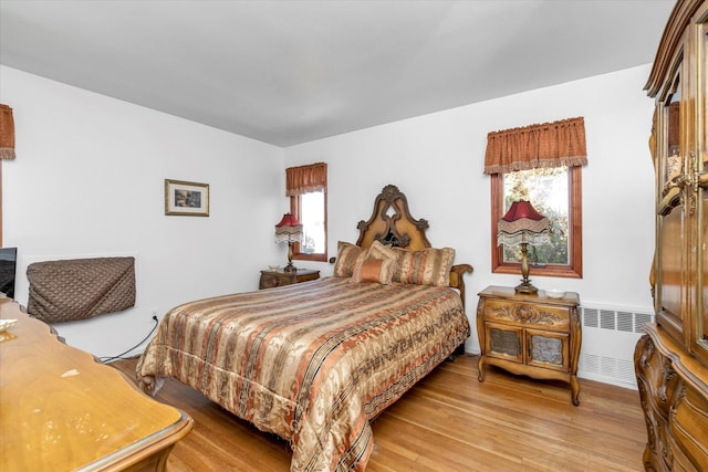 bedroom with radiator heating unit, multiple windows, and light wood-type flooring