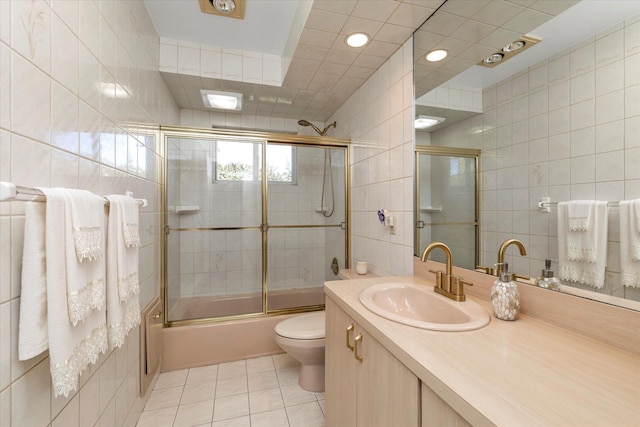 full bathroom with combined bath / shower with glass door, tile walls, vanity, toilet, and tile patterned floors