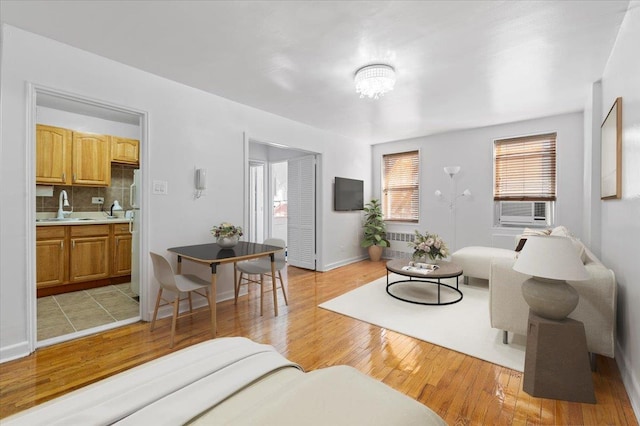 living room with radiator, an inviting chandelier, light wood-type flooring, cooling unit, and sink