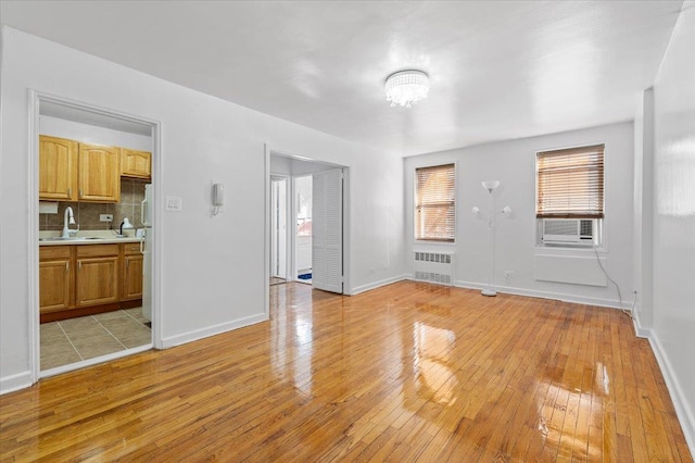 unfurnished living room with sink, cooling unit, radiator heating unit, and light wood-type flooring