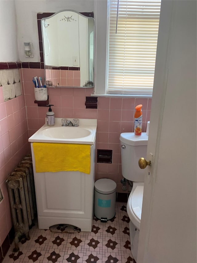 bathroom with radiator heating unit, tile patterned floors, tile walls, toilet, and vanity