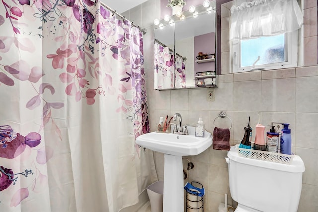 bathroom featuring toilet, tasteful backsplash, tile walls, walk in shower, and sink