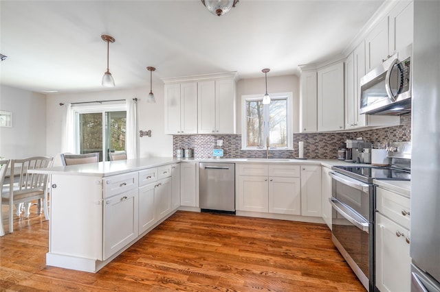 kitchen with appliances with stainless steel finishes, pendant lighting, white cabinets, and kitchen peninsula