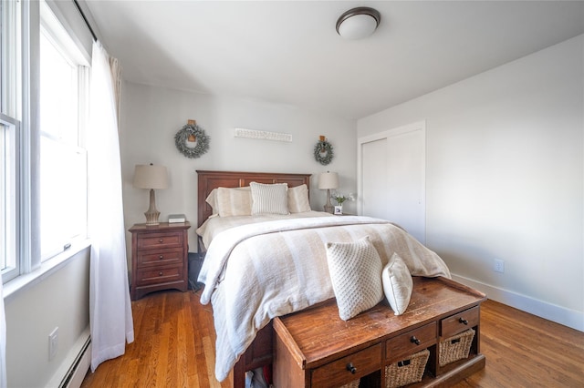 bedroom with a baseboard heating unit, a closet, multiple windows, and wood-type flooring