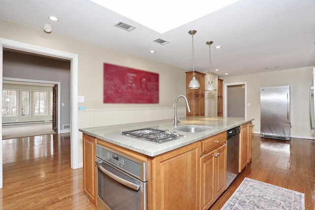 kitchen featuring a kitchen island with sink, light hardwood / wood-style floors, stainless steel appliances, hanging light fixtures, and sink