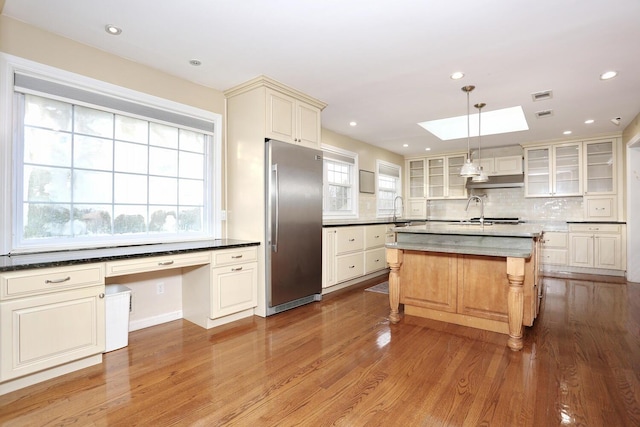 kitchen with decorative light fixtures, a kitchen island with sink, a skylight, a breakfast bar area, and stainless steel built in refrigerator