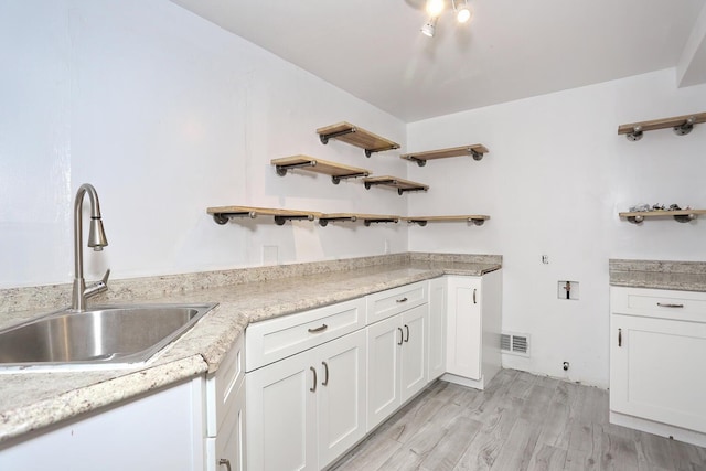 kitchen with sink, white cabinets, light wood-type flooring, and light stone countertops