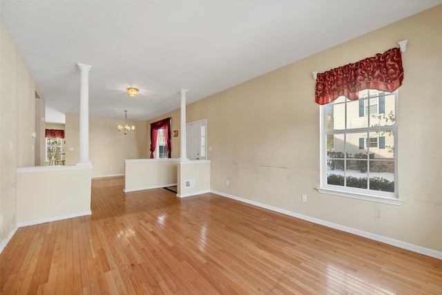 unfurnished living room featuring light hardwood / wood-style floors, a chandelier, and ornate columns