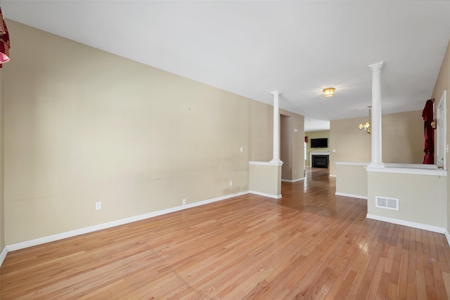 unfurnished living room featuring decorative columns and light wood-type flooring