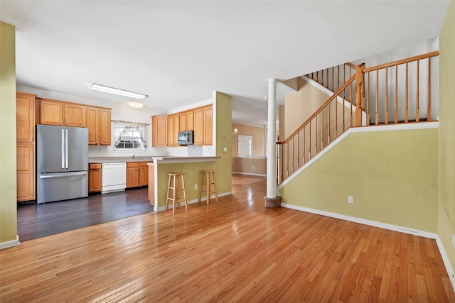 kitchen with sink, a breakfast bar area, light hardwood / wood-style flooring, appliances with stainless steel finishes, and kitchen peninsula