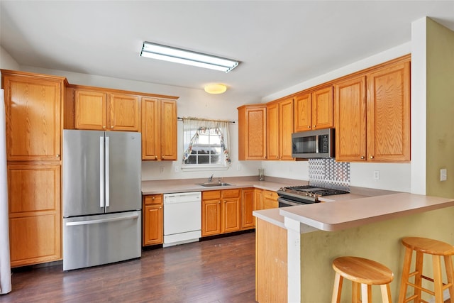 kitchen with dark wood-type flooring, sink, appliances with stainless steel finishes, a kitchen breakfast bar, and kitchen peninsula