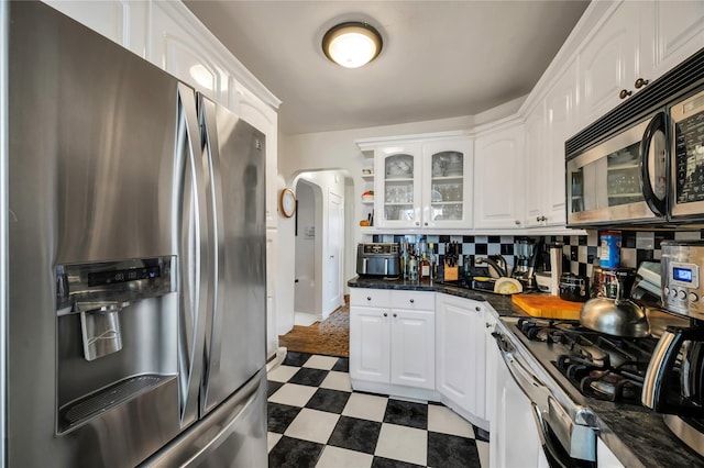 kitchen featuring stainless steel appliances, white cabinetry, tasteful backsplash, and dark stone countertops