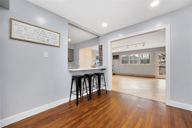 kitchen with hardwood / wood-style floors, a kitchen bar, kitchen peninsula, and a baseboard heating unit