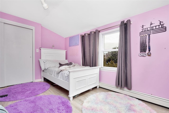 bedroom with baseboard heating, light wood-type flooring, vaulted ceiling, and a closet