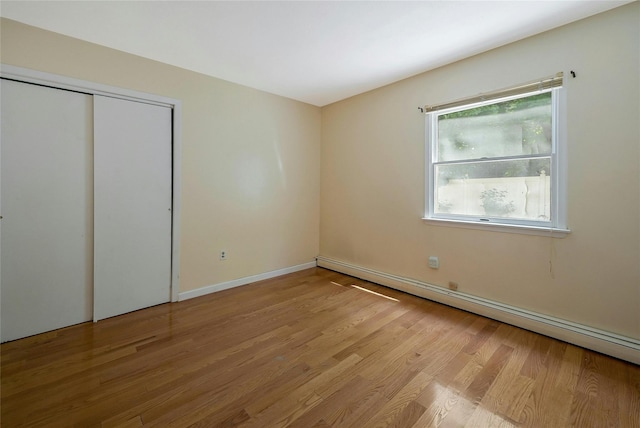 unfurnished bedroom with baseboard heating, light wood-type flooring, and a closet