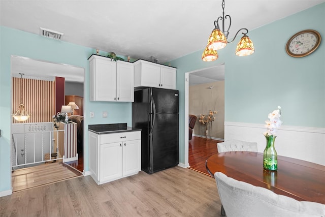 kitchen featuring black refrigerator, light wood-type flooring, white cabinetry, and pendant lighting