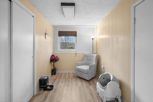 sitting room with a textured ceiling, light hardwood / wood-style flooring, and wood walls