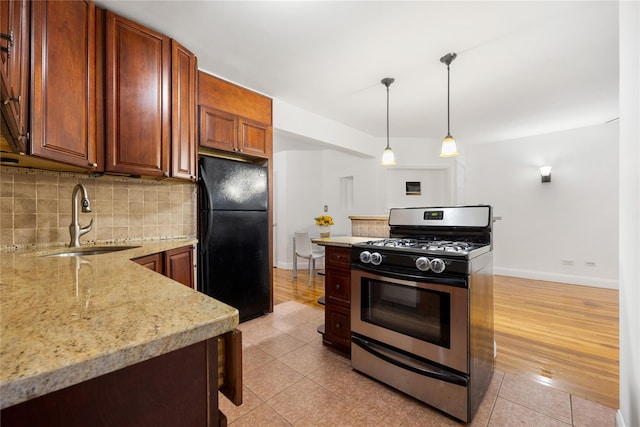 kitchen featuring black refrigerator, hanging light fixtures, gas stove, sink, and backsplash