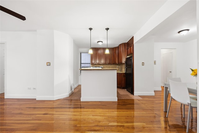 kitchen featuring black fridge, light wood-type flooring, backsplash, and pendant lighting