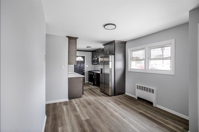 kitchen with stainless steel appliances, radiator heating unit, dark brown cabinets, and light hardwood / wood-style flooring