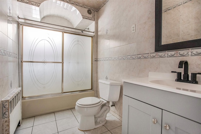 full bathroom with tile walls, toilet, radiator heating unit, and combined bath / shower with glass door